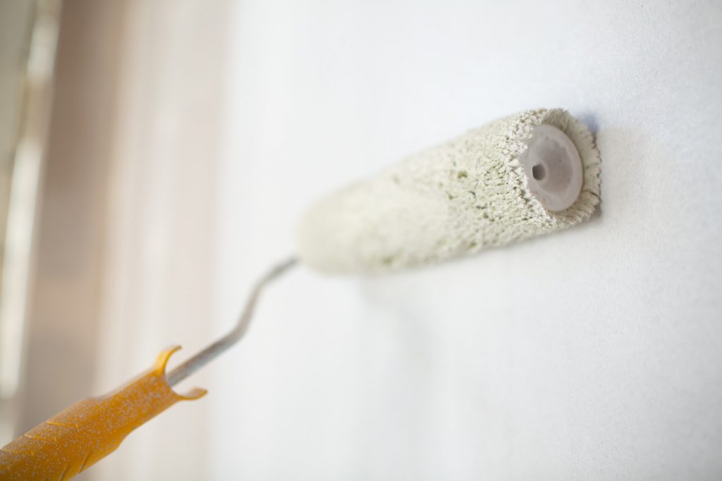 White paint roller in hand with drywall wall