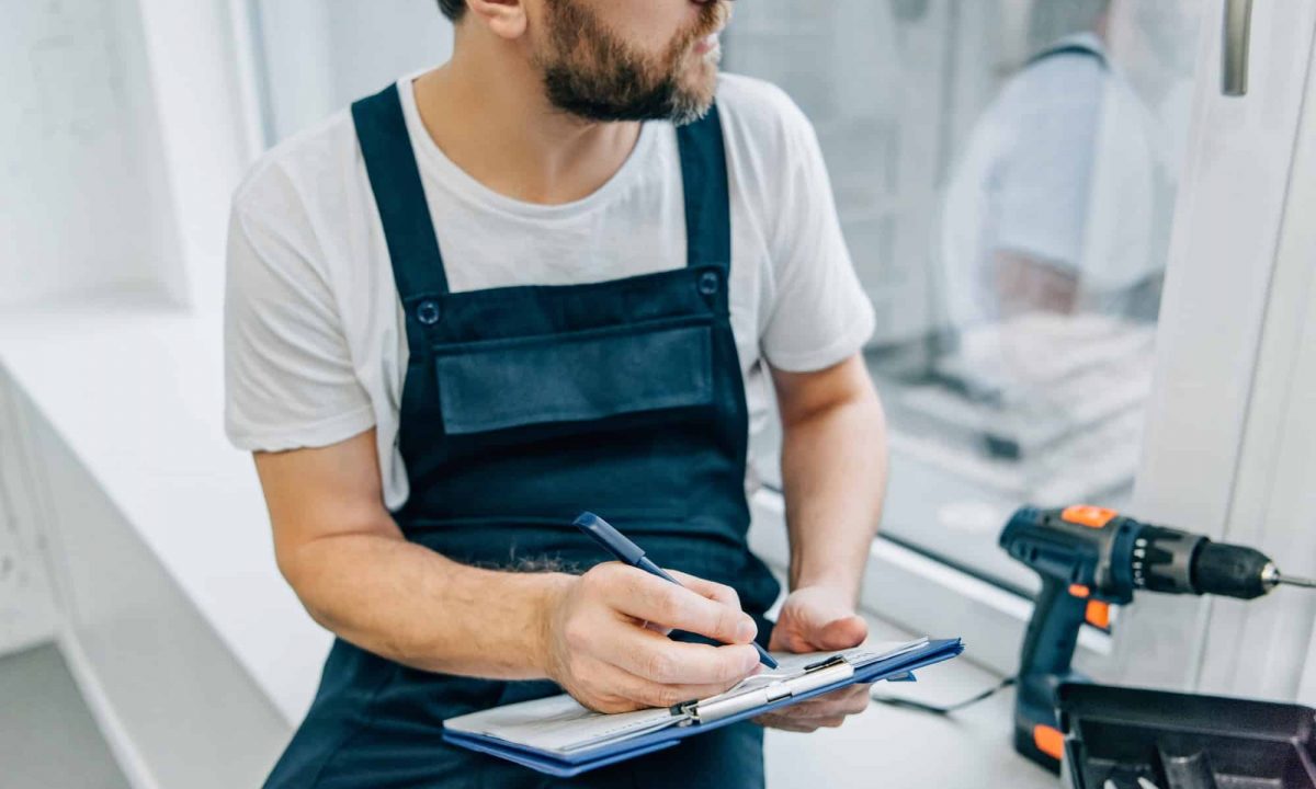 partial view of male handyman writing in clipboard and checking window